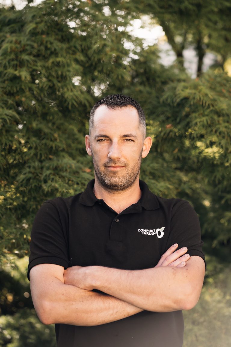 Portrait de Benjamin Egret, paysagiste CONFORT O JARDIN, bras croisés devant un conifère