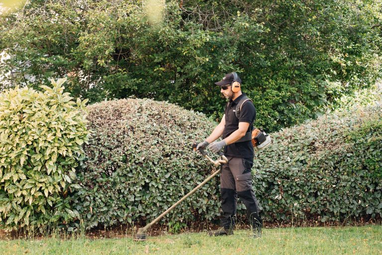 Benjamin Egret passe la débroussailleuse le long d’une haie dans un parc