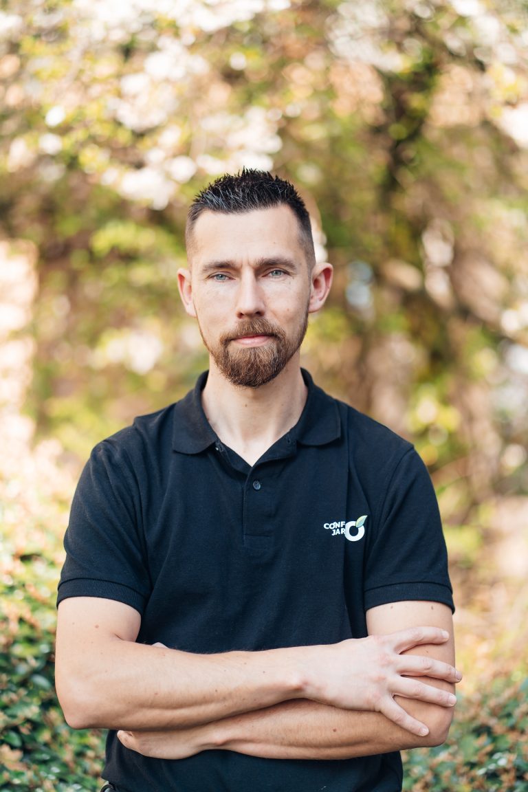 Portrait de Stéphane, paysagiste CONFORT O JARDIN, bras croisés devant un feuillage