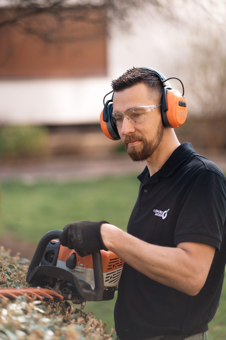 Stéphane, lunettes de protection et casque antibruit, taille une haie au taille-haie thermique