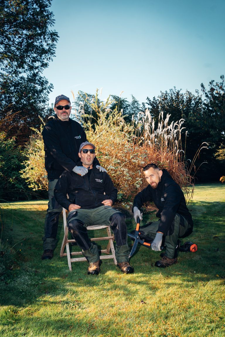 Renaud, Benjamin Egret et Stéphane posent dans un jardin, l’un assis sur un tabouret en bois