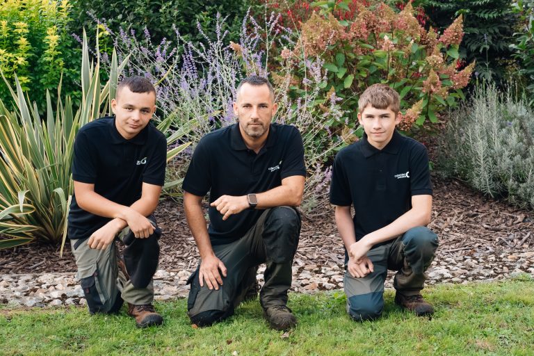 Yoni, Benjamin Egret et Louka accroupis devant un massif de vivaces et de graminées