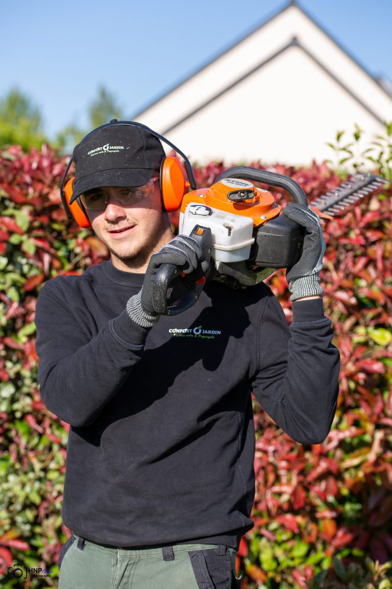 Noel présente son taille-haie thermique STIHL devant une haie de photinias rouges