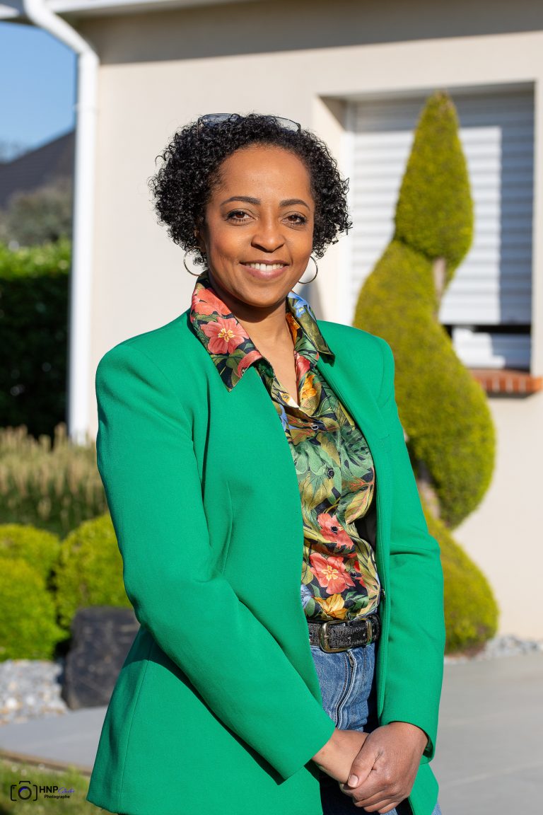 Samira, assistante administrative et commerciale de CONFORT O JARDIN, en veste verte devant un jardin paysager