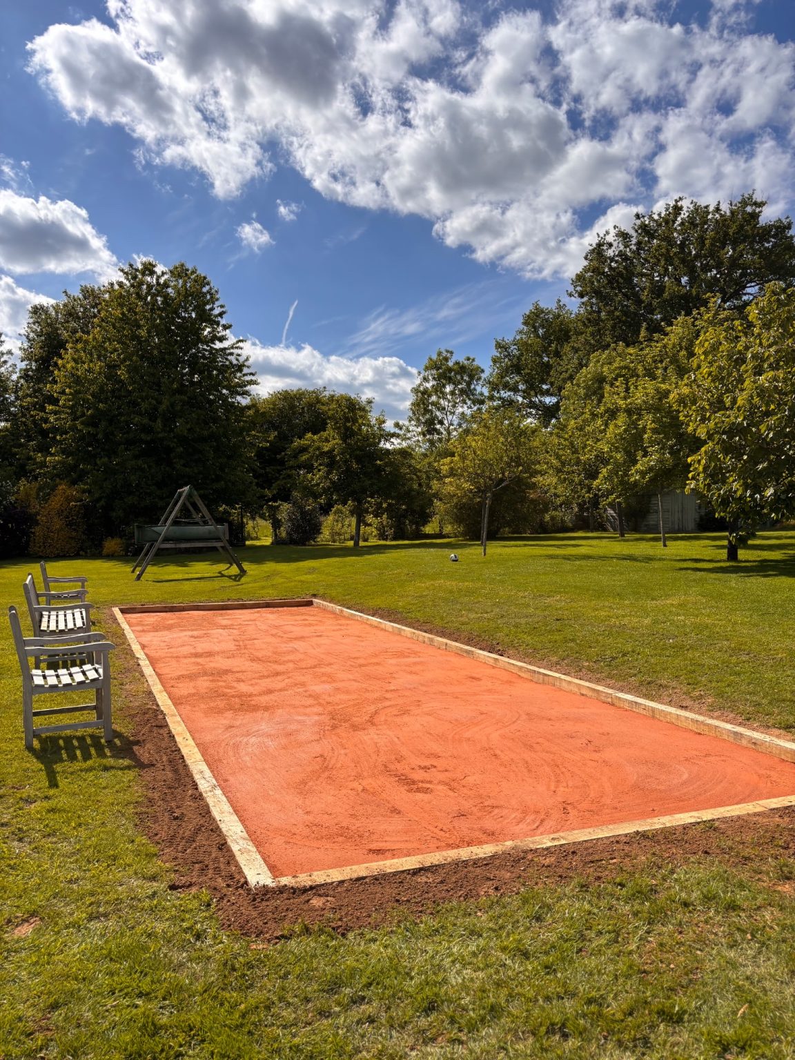 Terrain de pétanque terminé bordé de madriers, avec bancs, au milieu d'une pelouse arborée