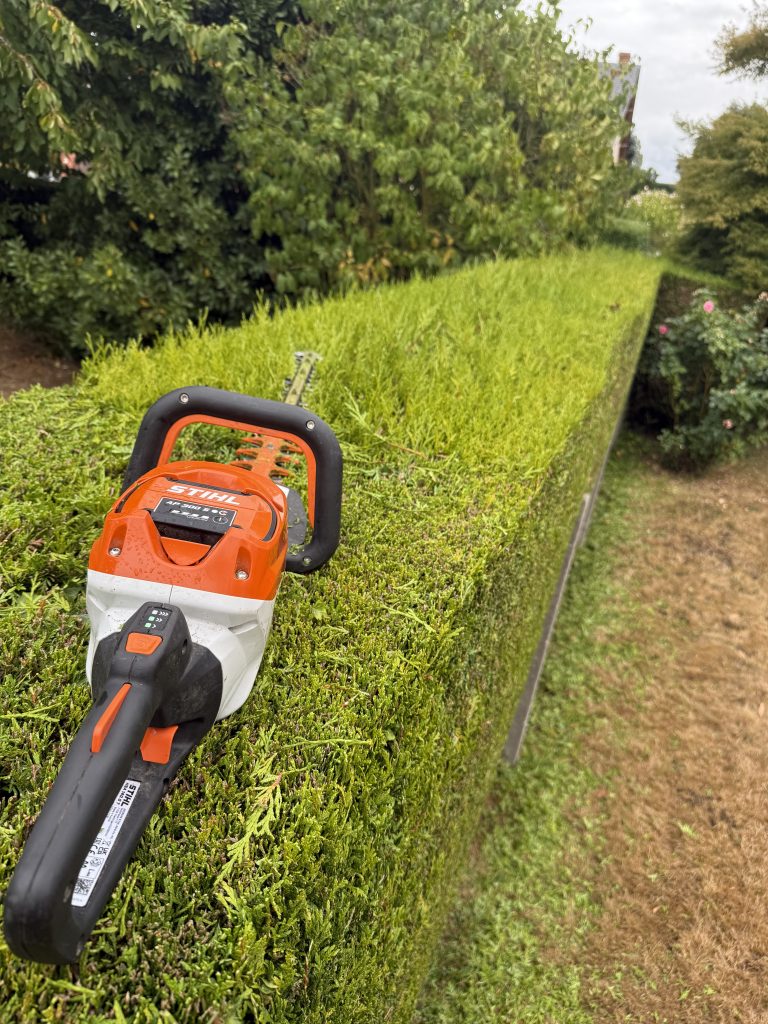 Taille-haie sur batterie STIHL posé sur le dessus d'une haie fraîchement taillée